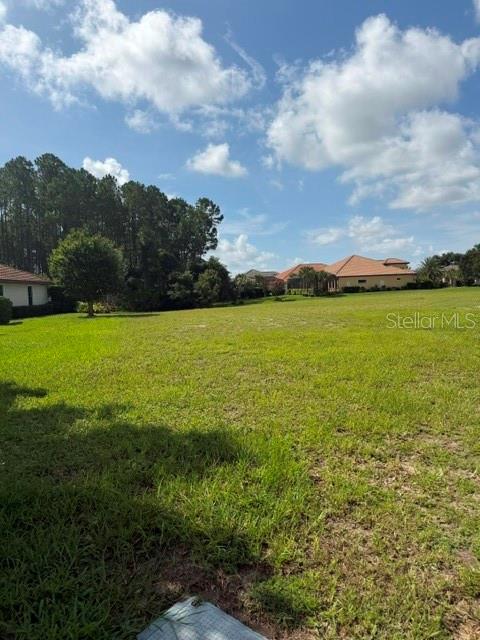 A large, grassy vacant lot with trees in the background under a cloudy blue sky — 515 SWEETGUM LANE LANE, PALM COAST, FL