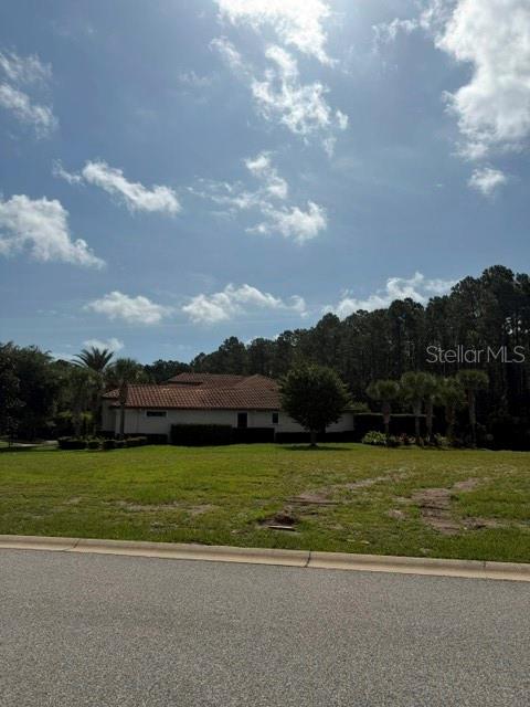 A view of a vacant grassy lot with a house and trees in the background — 515 SWEETGUM LANE LANE, PALM COAST, FL