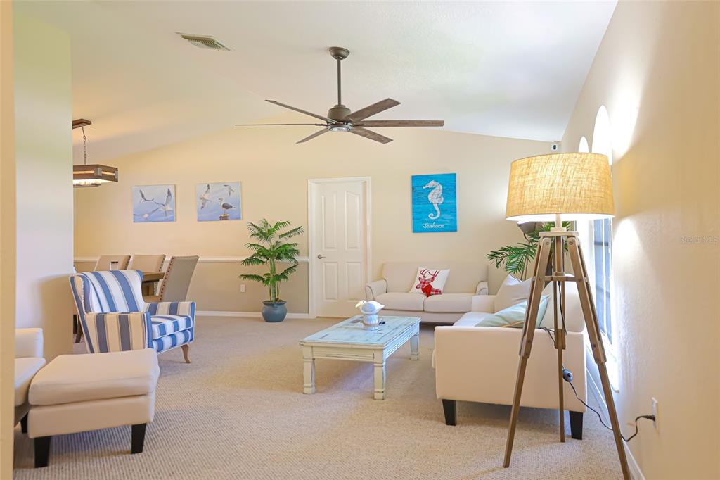 A living room features beige walls, a ceiling fan, a tripod lamp, and coastal decor — 1690 WAXWING COURT, VENICE, FL
