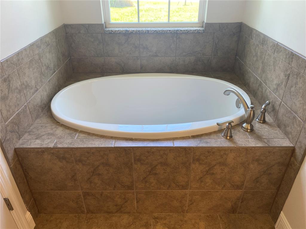 An oval soaking tub is set into a tiled deck beneath a window in a bathroom — 1828 SPANIEL AVENUE, NORTH PORT, FL