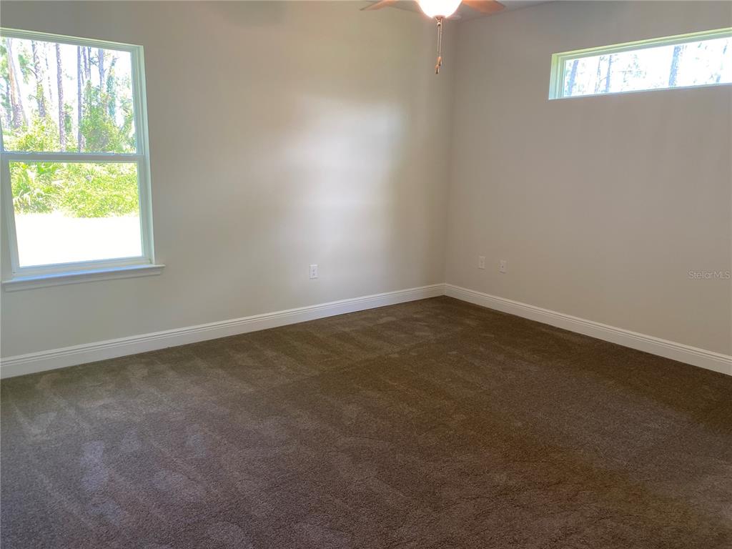 An empty bedroom features beige walls, brown carpeting, a ceiling fan, and two windows — 1828 SPANIEL AVENUE, NORTH PORT, FL