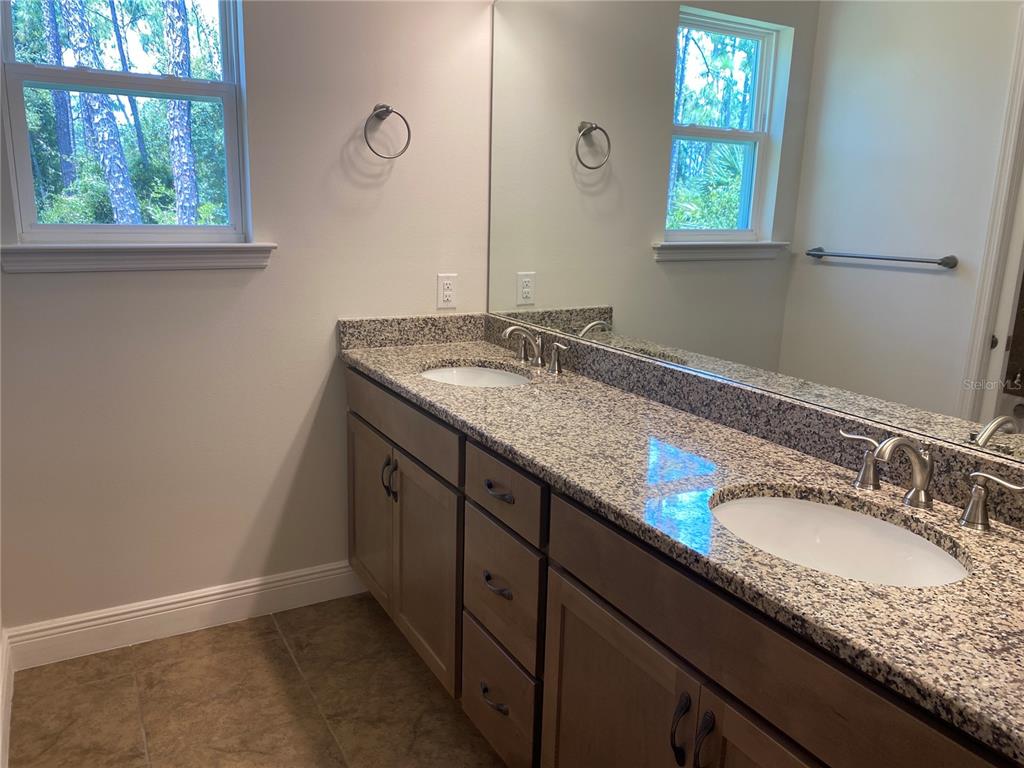A bathroom features a double-sink granite vanity with wooden cabinets and a large wall mirror — 1828 SPANIEL AVENUE, NORTH PORT, FL