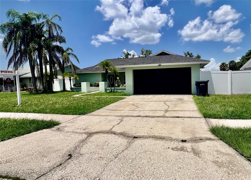 A light green house with a dark garage door and palm trees in the front yard — 10902 WINGATE DRIVE, TAMPA, FL