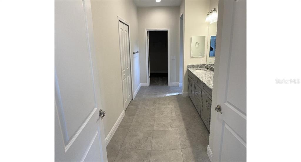 A bathroom with gray cabinetry, a granite countertop, and tile flooring leads to a closet — 1189 DELMONTE STREET, NORTH PORT, FL