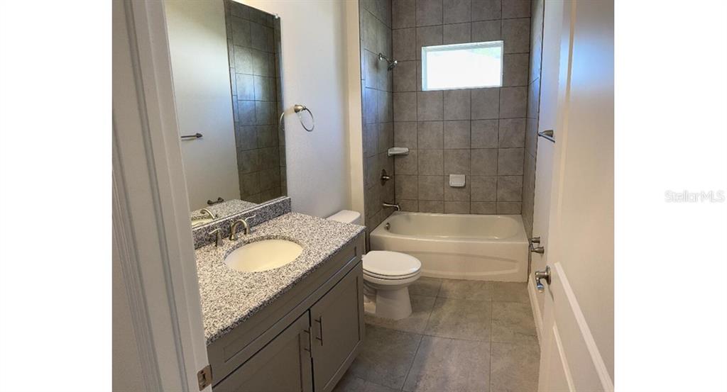A bathroom features a gray vanity with a granite countertop, a toilet, and a tiled tub — 1189 DELMONTE STREET, NORTH PORT, FL