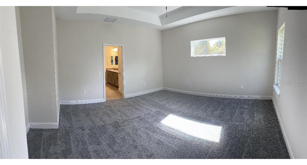 A spacious bedroom with gray carpet, a tray ceiling, and an open doorway to a bathroom — 1189 DELMONTE STREET, NORTH PORT, FL
