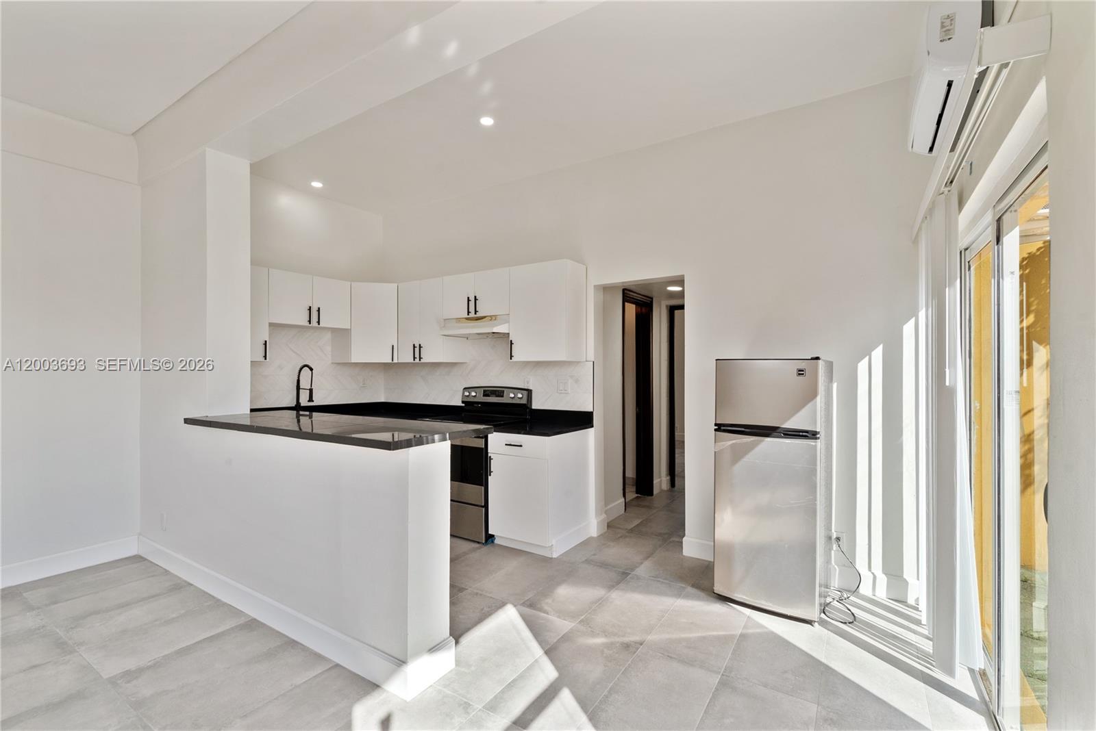 A modern kitchen features white cabinets, black countertops, stainless steel appliances, and gray tile flooring — 2204 Mckinley St, Hollywood FL 33020, HOLLYWOOD, FL