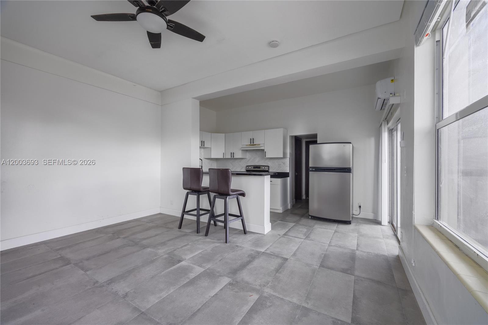A kitchen with white cabinets and a breakfast bar opens into a tiled living area — 2204 Mckinley St, Hollywood FL 33020, HOLLYWOOD, FL