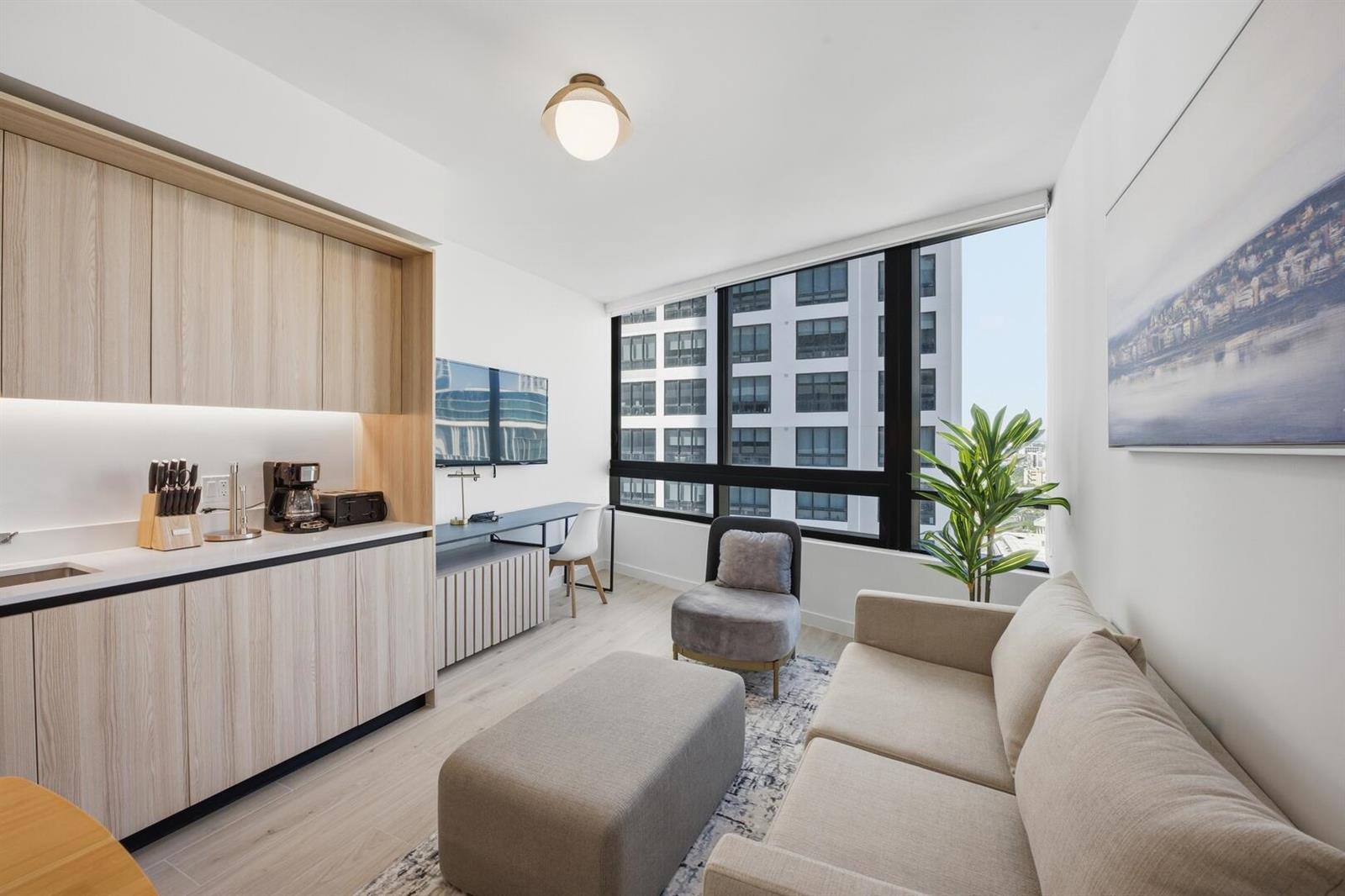 A modern studio apartment features a kitchenette, a sofa, and floor-to-ceiling windows overlooking buildings — 225 N Miami Avenue # 2002, Miami FL 33128, MIAMI, FL