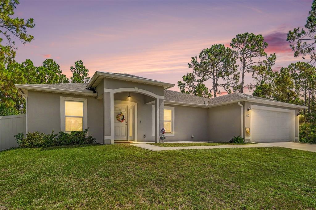 A single-story house with a gray exterior, arched entryway, and attached garage at dusk — 427 SE FLAGLER RD, PALM BAY, FL