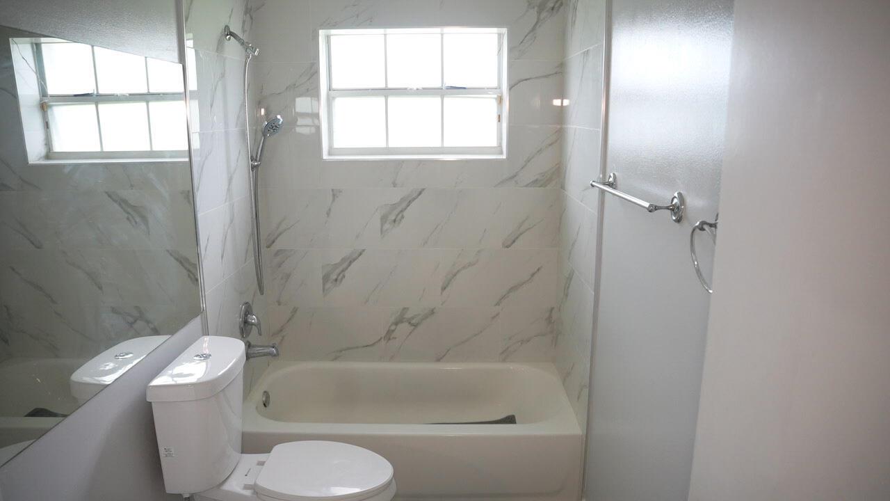 A bathroom features a white bathtub, a toilet, and marble-patterned tile walls — 201 Maplewood Drive # 201, FL 33415, FL