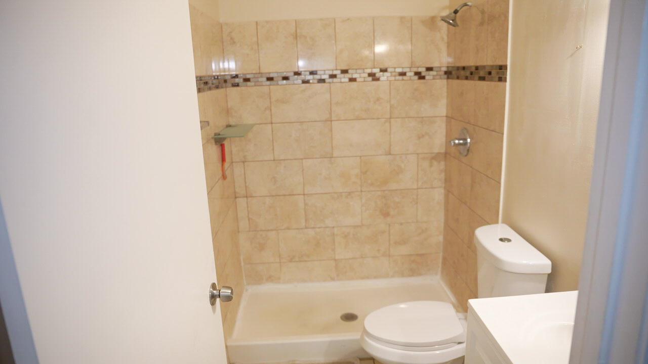 A bathroom features a tiled shower stall with a glass shelf and a white toilet — 201 Maplewood Drive # 201, FL 33415, FL