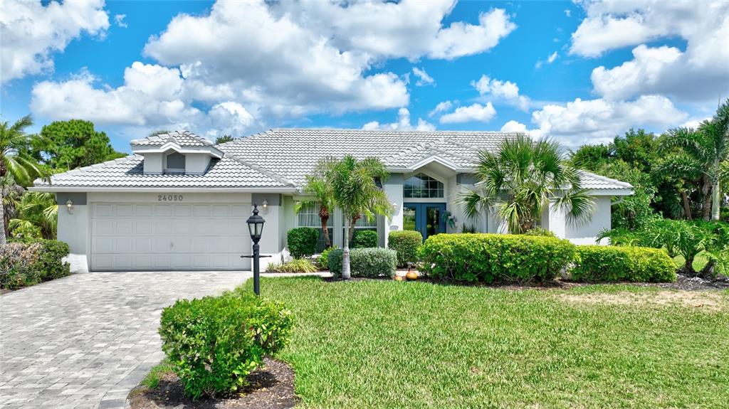A single-story house with a tiled roof, a two-car garage, and a landscaped front yard — 24050 REDFISH COVE DRIVE, PUNTA GORDA, FL