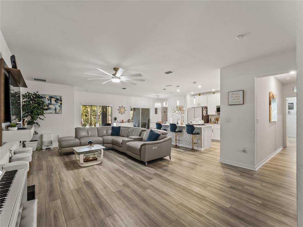 An open-concept living room and kitchen featuring light wood flooring and a gray sectional sofa — 1367 MILIKEN TERRACE, PORT CHARLOTTE, FL