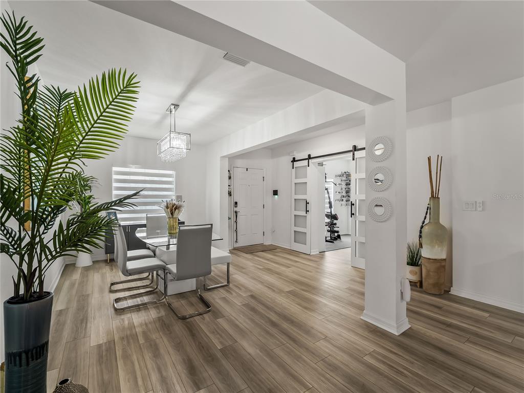 A dining area with a glass table, modern chairs, and a sliding barn door entrance — 1367 MILIKEN TERRACE, PORT CHARLOTTE, FL