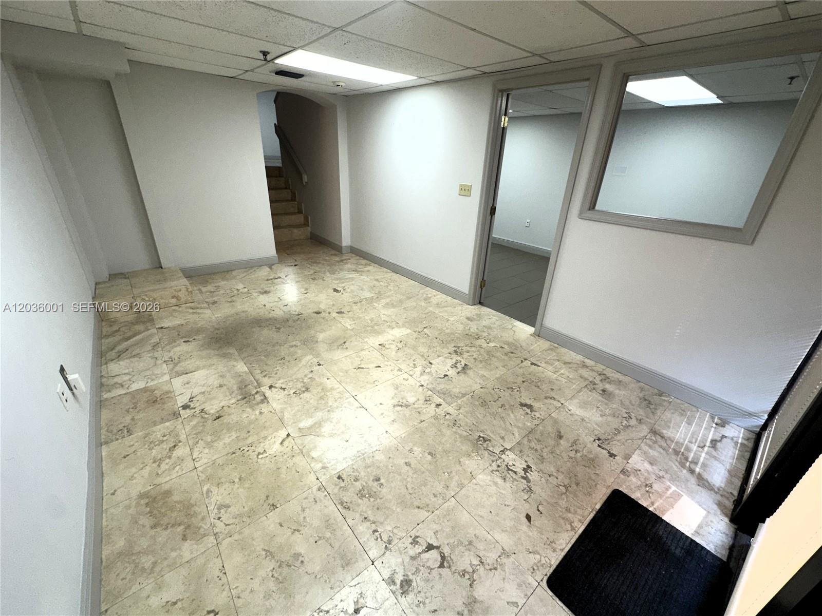 A room with beige tile flooring, a drop ceiling, and a doorway leading to stairs — 7038 NW 50th St # 2, Miami FL 33166, MIAMI, FL
