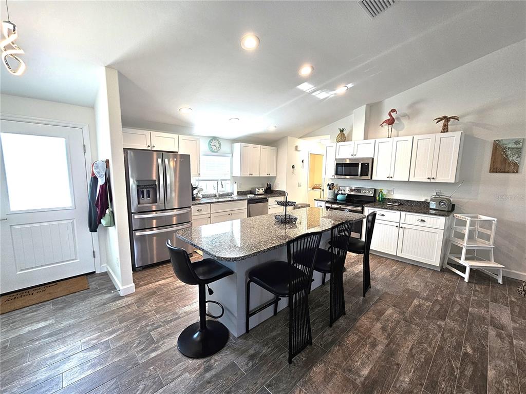 A kitchen features white cabinets, granite countertops, a central island with stools, and wood-look flooring — 7436 MICHAEL STREET, ENGLEWOOD, FL