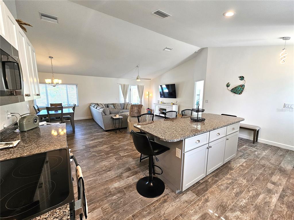 An open-concept kitchen and living area featuring granite countertops, white cabinetry, and wood-look tile flooring — 7436 MICHAEL STREET, ENGLEWOOD, FL