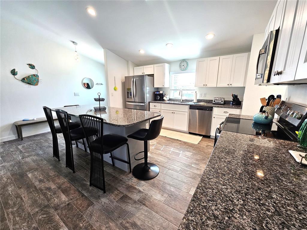 A kitchen features white cabinets, granite countertops, a center island with seating, and wood-look flooring — 7436 MICHAEL STREET, ENGLEWOOD, FL