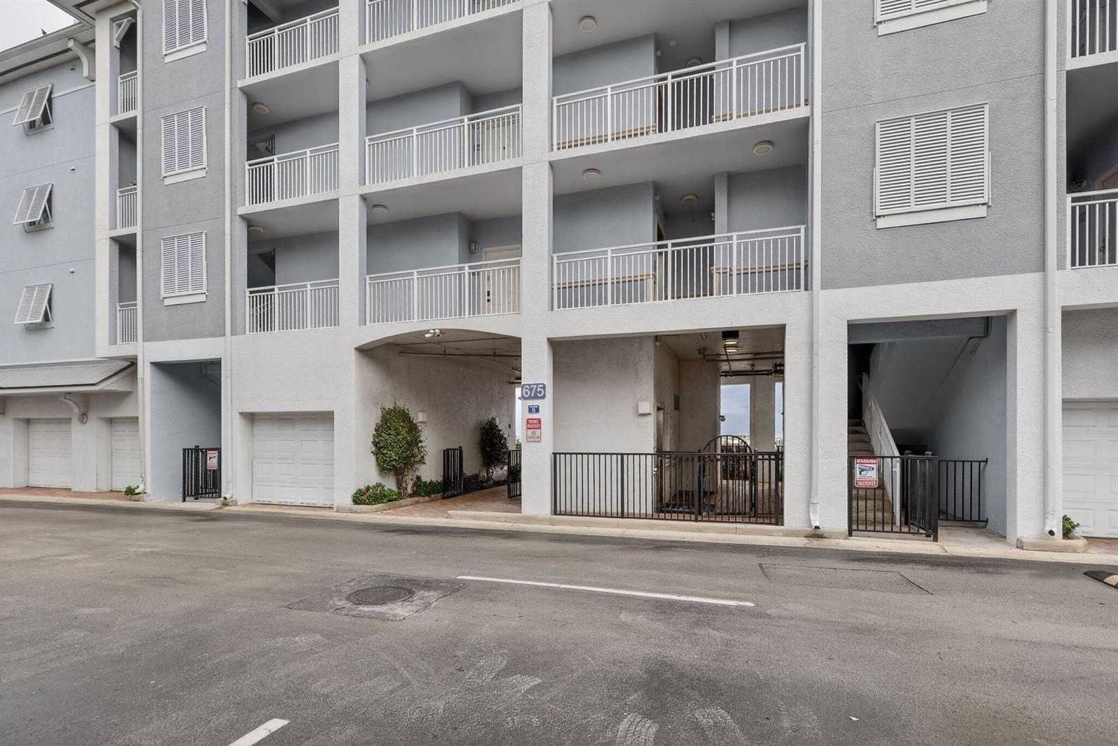 The exterior of a multi-story apartment building features balconies, white railings, and ground-level parking bays — 675 NW Flagler Avenue Unit 202, Stuart FL 34994, STUART, FL