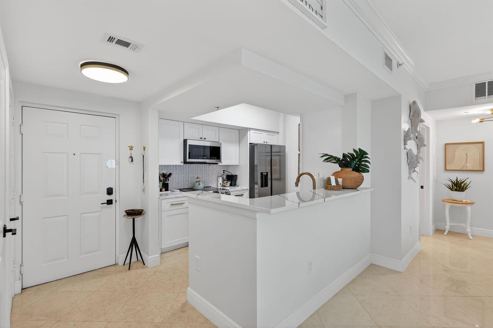 A white kitchen with a breakfast bar, stainless steel appliances, and tile flooring — 675 NW Flagler Avenue Unit 202, Stuart FL 34994, STUART, FL