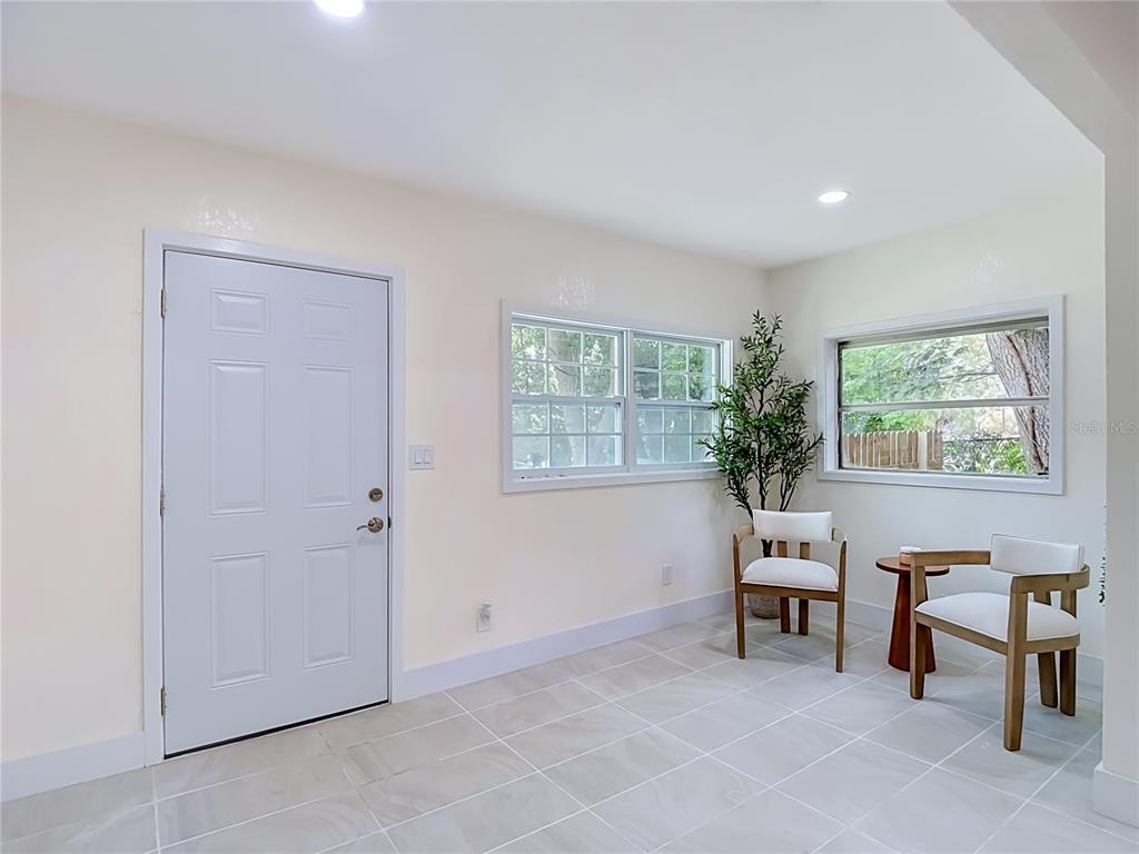 A bright entryway features white walls, light tile flooring, two windows, and two wooden chairs — 8010 N 13TH STREET, TAMPA, FL