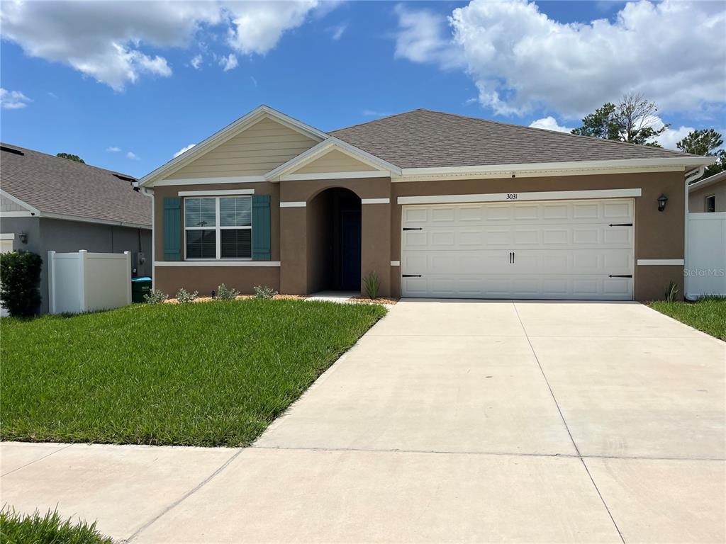 A single-story house with a brown stucco exterior, a two-car garage, and a front lawn — 3031 STATEN DRIVE, DELTONA, FL