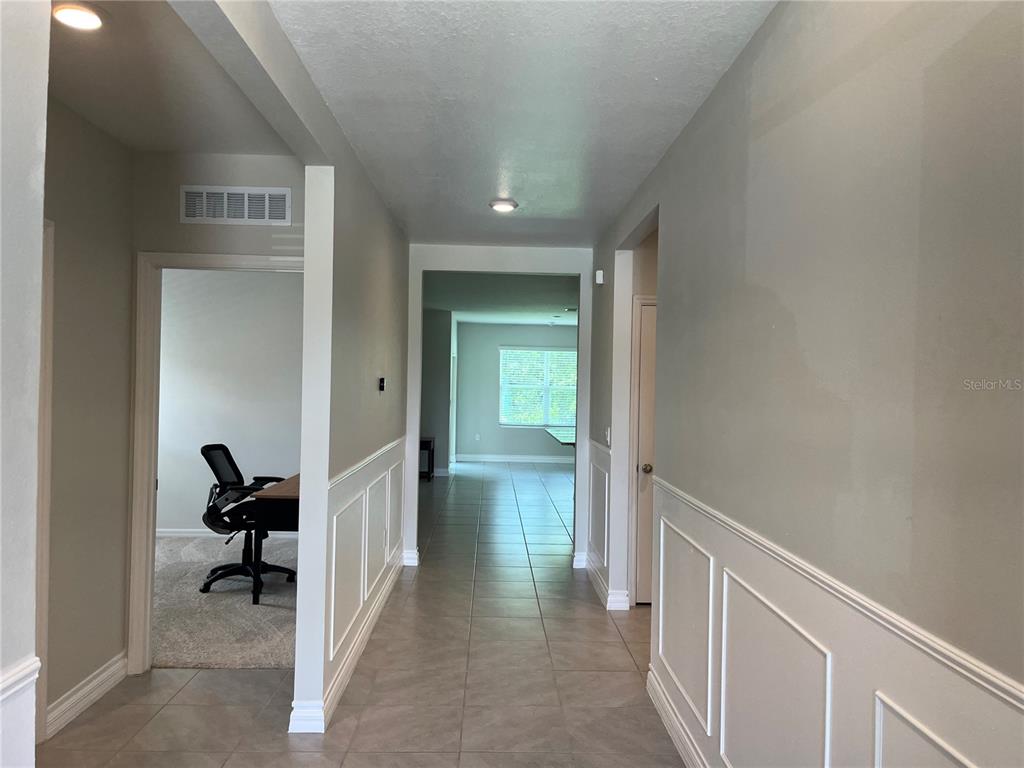 A hallway with tile flooring and wainscoting leads to a room with a desk — 3031 STATEN DRIVE, DELTONA, FL