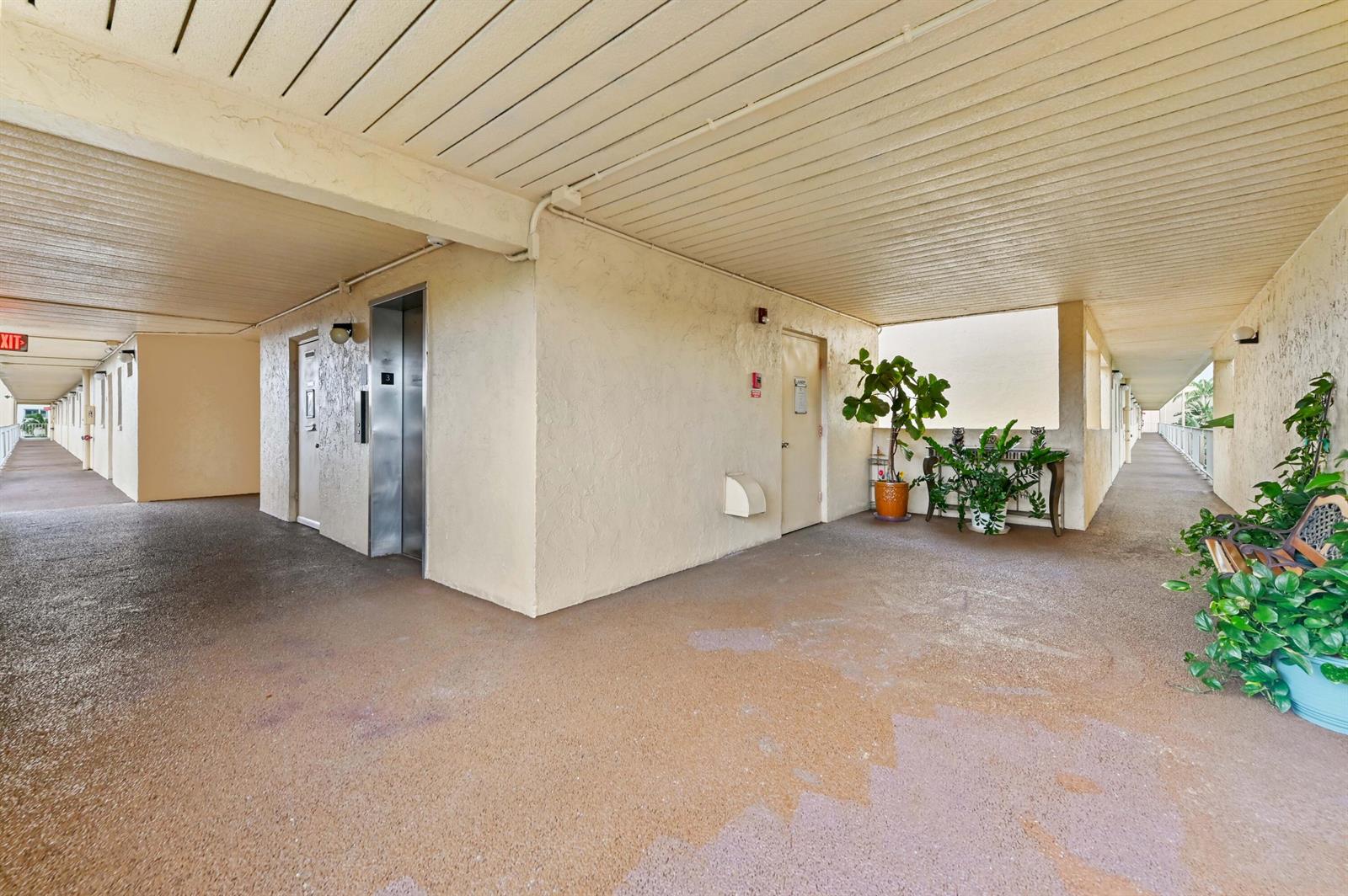 An outdoor apartment building hallway features an elevator, a door, and potted plants — 2615 NE 3rd Court # 3170, Boynton Beach FL 33435, BOYNTON BEACH, FL