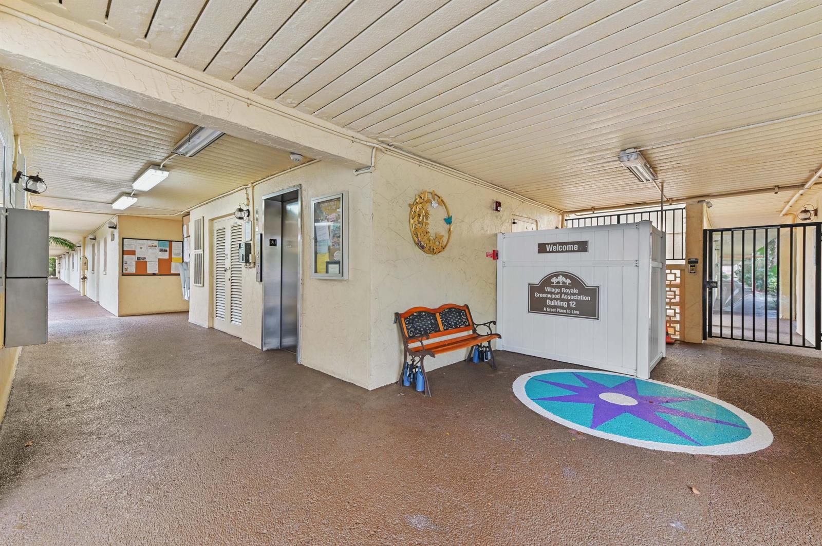 An outdoor covered entryway features an elevator, a bench, and a building identification sign — 2615 NE 3rd Court # 3170, Boynton Beach FL 33435, BOYNTON BEACH, FL