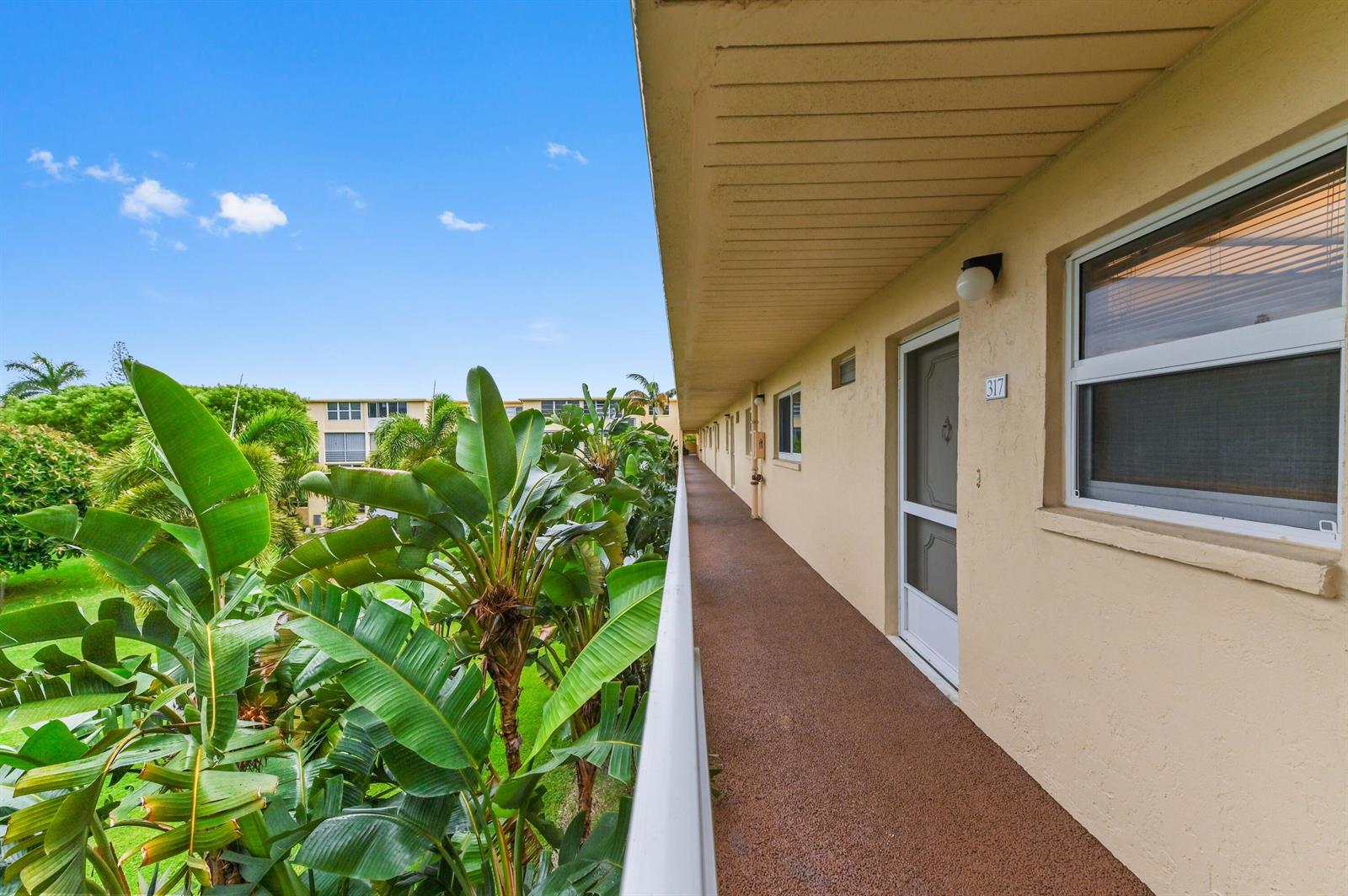 An exterior walkway with a brown textured floor overlooks lush tropical landscaping and palm trees — 2615 NE 3rd Court # 3170, Boynton Beach FL 33435, BOYNTON BEACH, FL