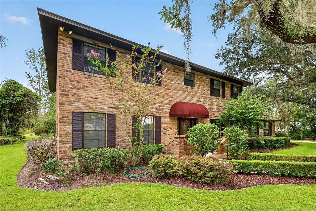 A two-story brick house features a red fabric awning over the front entrance — 15240 SHADY LANE, TAVARES, FL