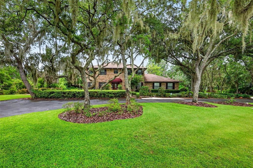 A two-story brick house sits behind a manicured lawn and large trees with Spanish moss — 15240 SHADY LANE, TAVARES, FL