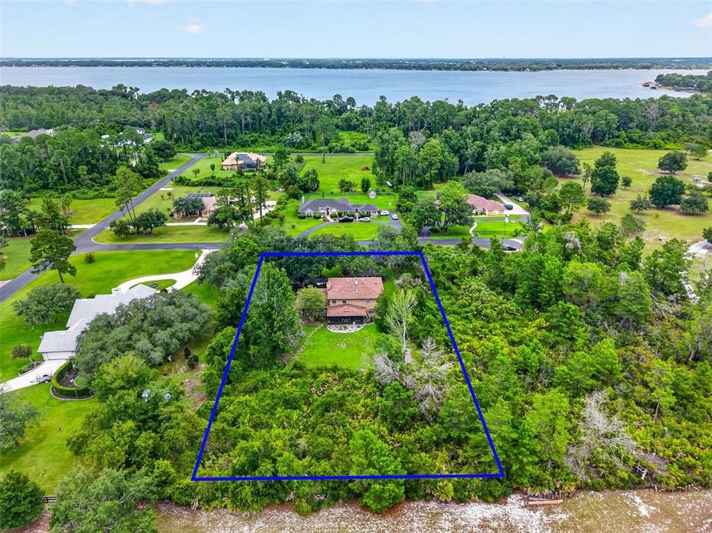 An aerial view shows a house on a wooded lot bordering a large body of water — 15240 SHADY LANE, TAVARES, FL