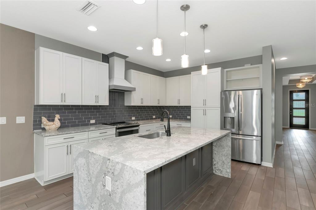 A modern kitchen features white cabinets, a gray tiled backsplash, and a large stone-topped island — 14941 BARROWS BLUFF TERRACE, BRADENTON, FL