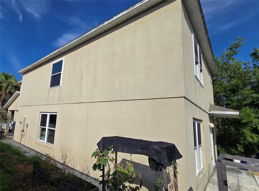 The exterior of a two-story beige stucco house features multiple windows and a small garden structure — 15108 HARROWGATE WAY, WINTER GARDEN, FL