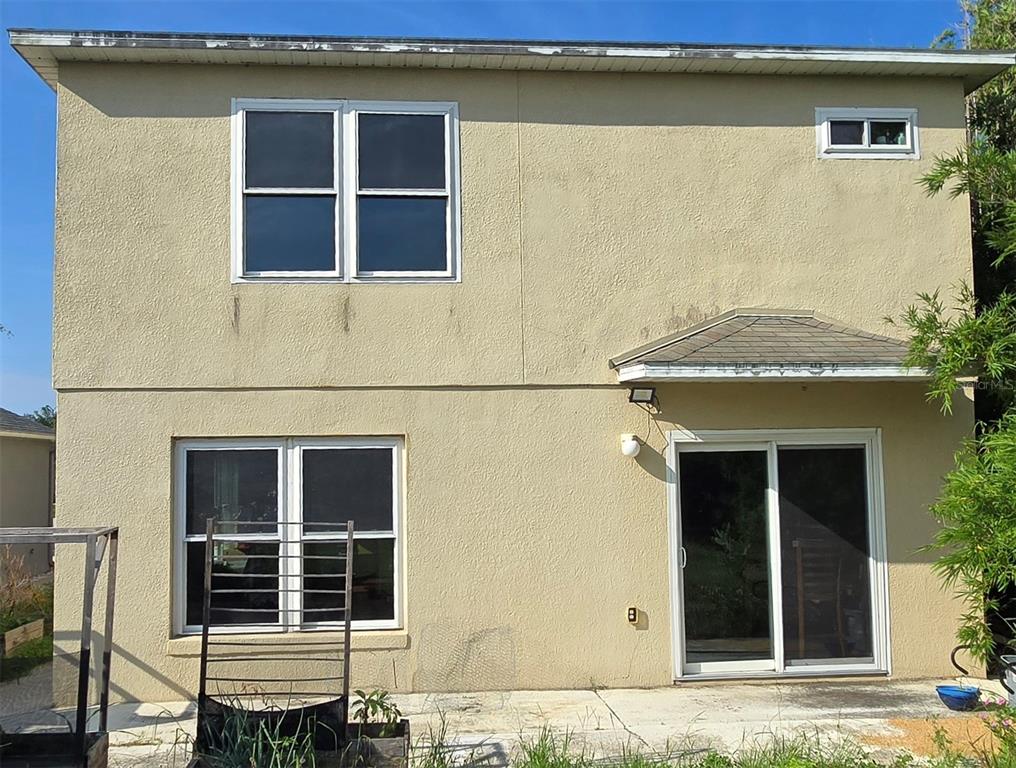 The exterior rear view of a two-story tan stucco house with a sliding glass door — 15108 HARROWGATE WAY, WINTER GARDEN, FL