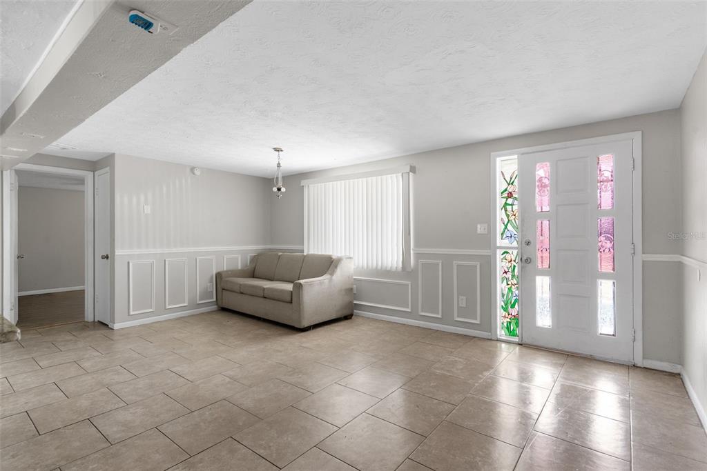 A living room with light tile flooring, a beige sofa, and a white front door — 2344 TAHITIAN DRIVE, HOLIDAY, FL