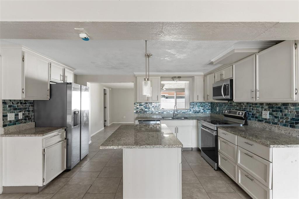 A kitchen with white cabinets, granite countertops, a central island, and blue tile backsplash — 2344 TAHITIAN DRIVE, HOLIDAY, FL