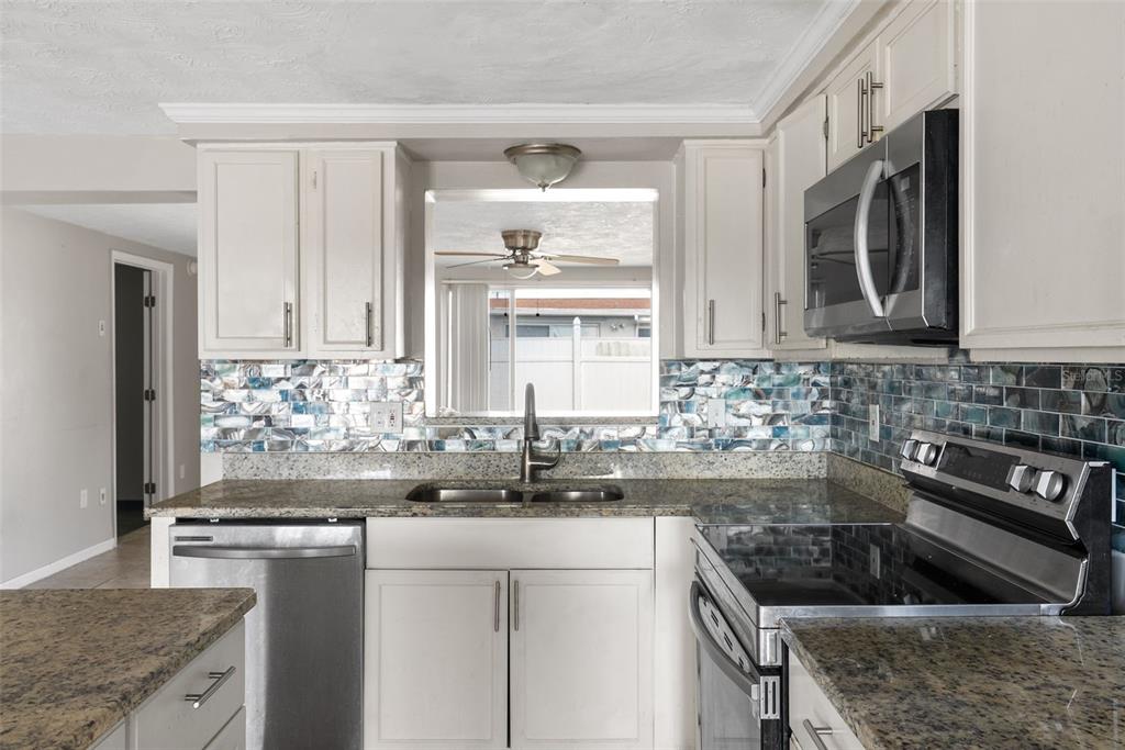 A kitchen features white cabinets, granite countertops, a stainless steel microwave, and a blue backsplash — 2344 TAHITIAN DRIVE, HOLIDAY, FL