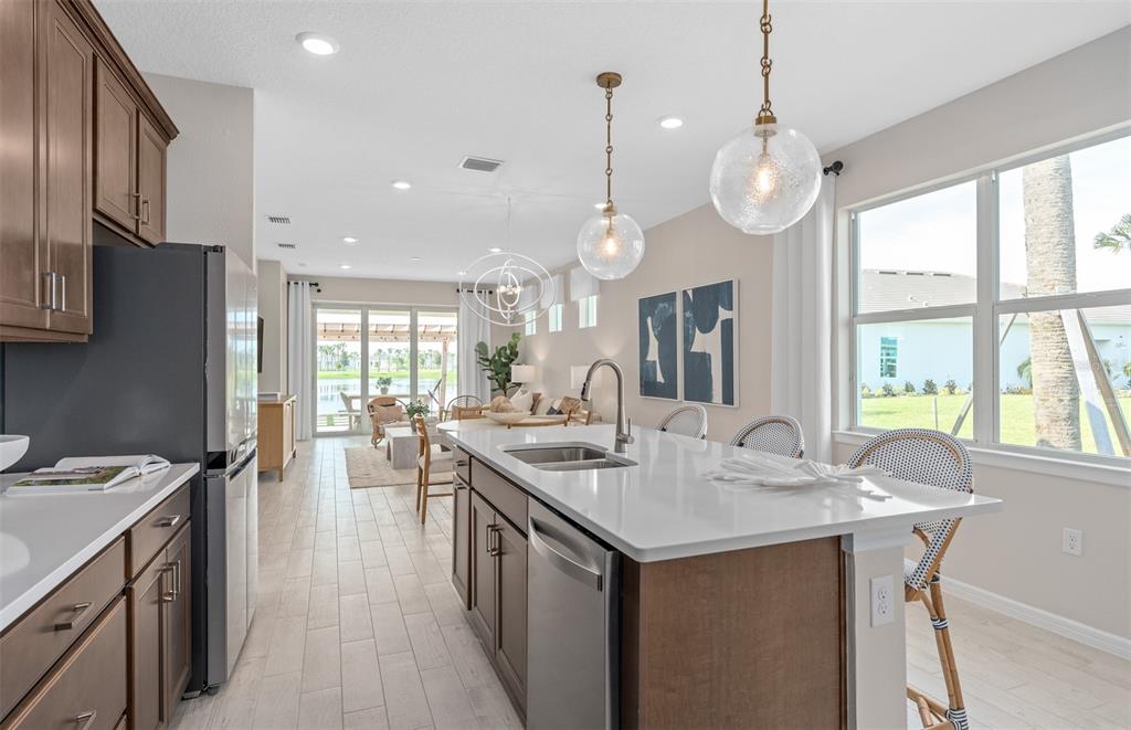 A kitchen with a white island, wooden cabinets, and stainless appliances opens to a living area — 3492 GUAVA PALMS COURT, VIERA, FL
