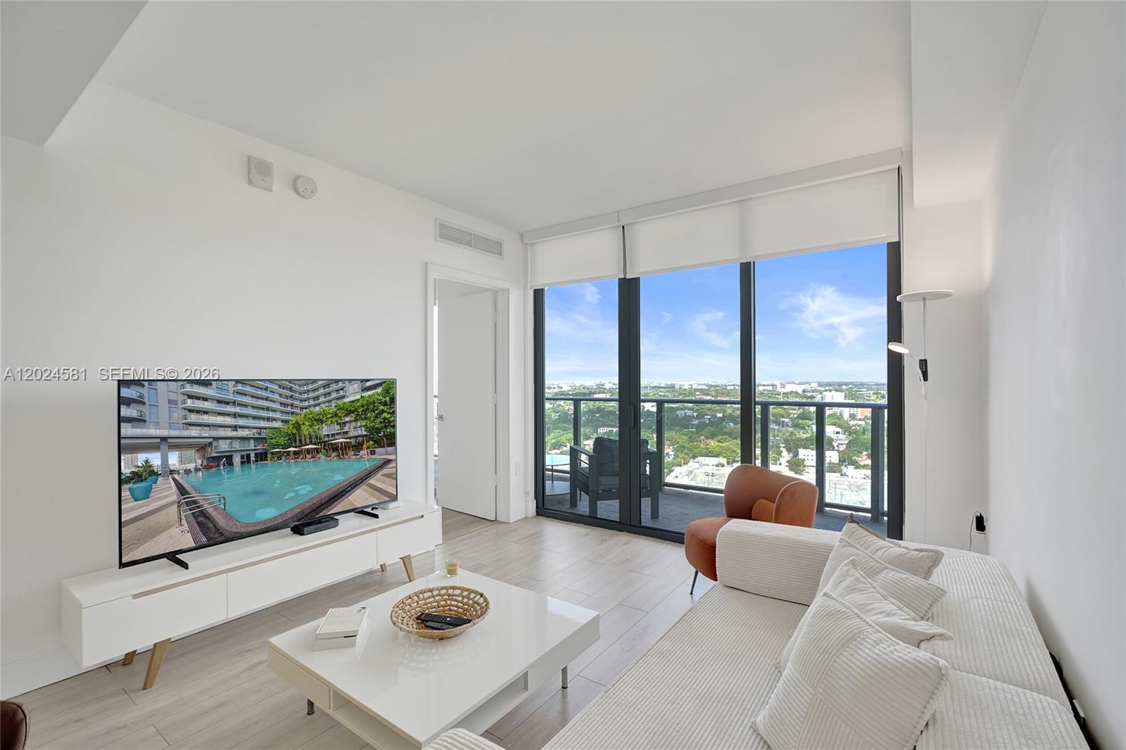 A modern living room features a white media console, a coffee table, and floor-to-ceiling windows — 121 NE 34th St # 2310, Miami FL 33137, MIAMI, FL