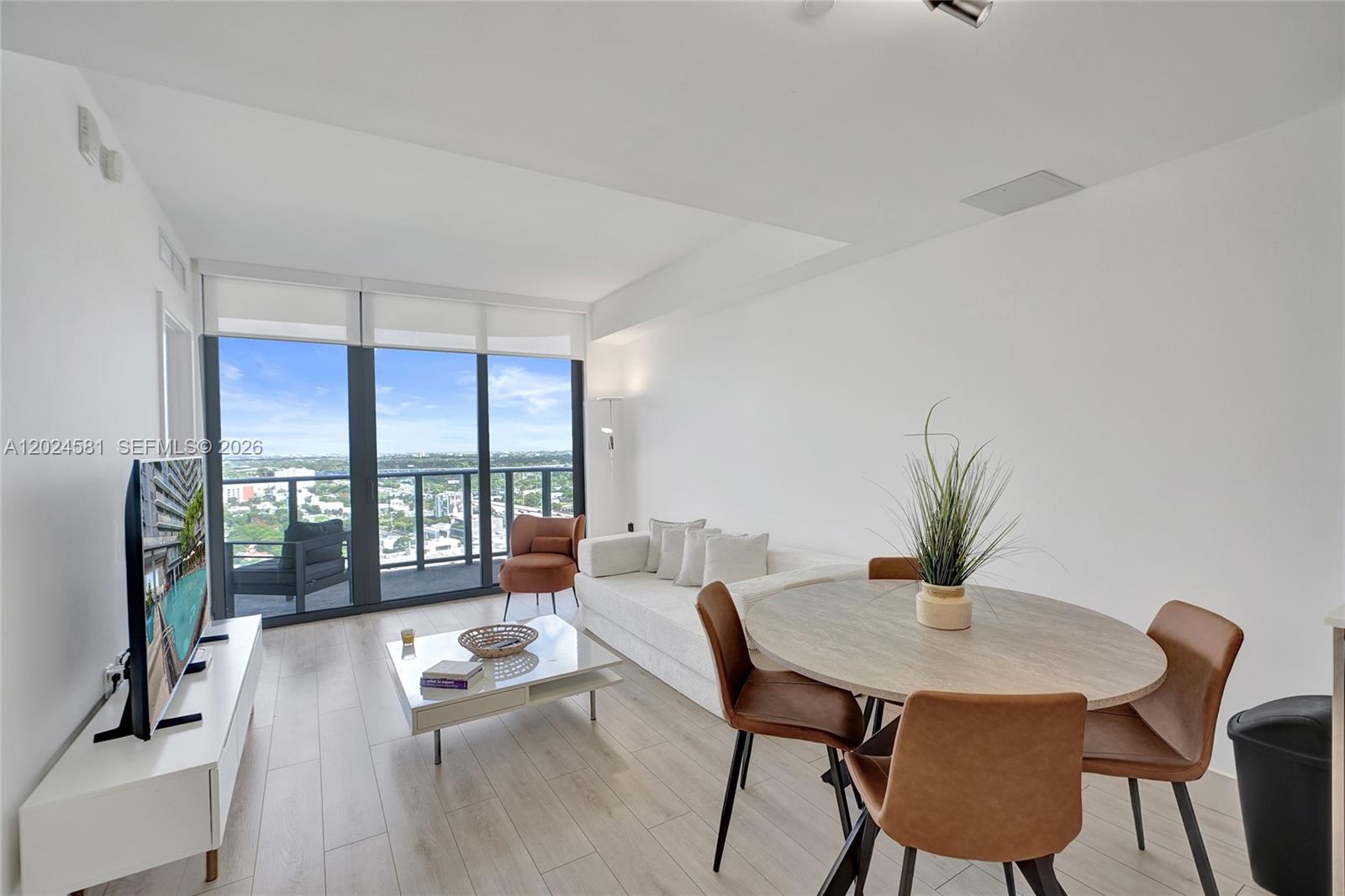 A living and dining area features light wood floors, a white sofa, and floor-to-ceiling windows — 121 NE 34th St # 2310, Miami FL 33137, MIAMI, FL