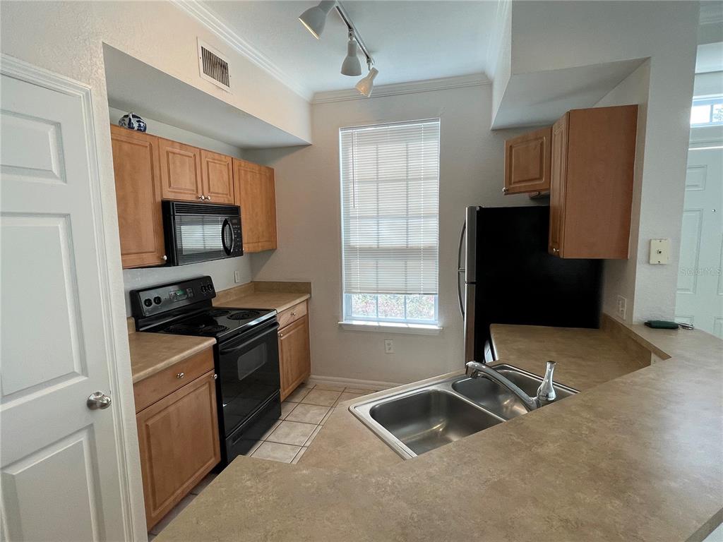A kitchen features light wood cabinets, black appliances, laminate countertops, and a double-basin sink — 5500 ROSEHILL ROAD UNIT 103, SARASOTA, FL