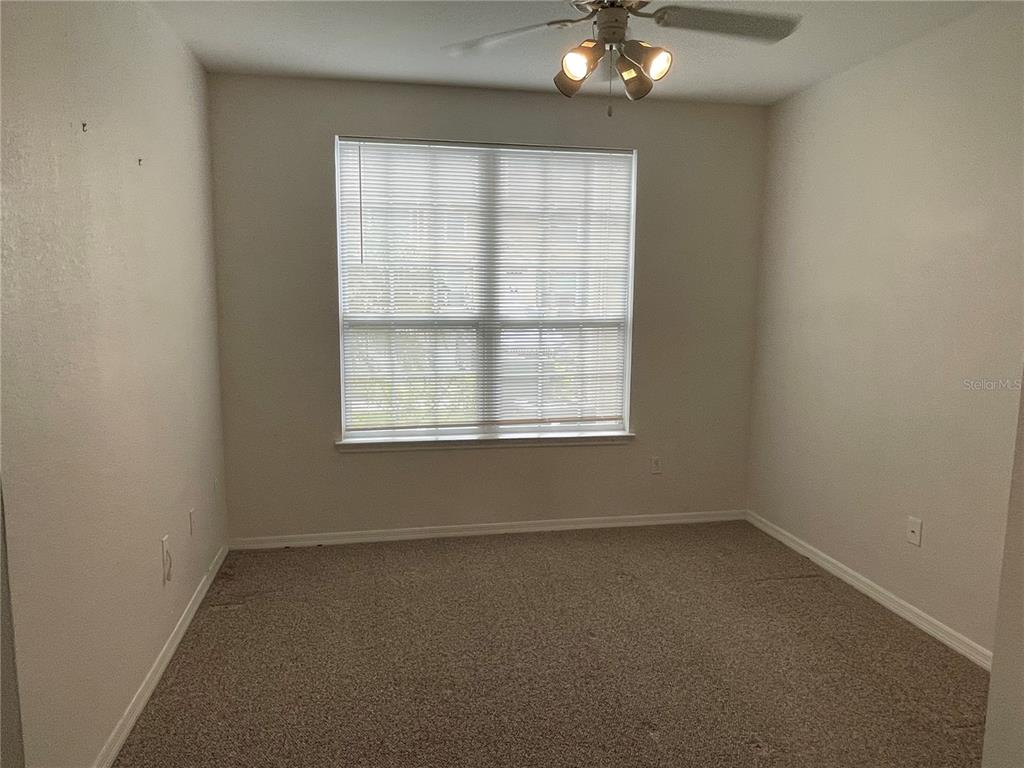 An empty bedroom features beige carpet, light-colored walls, a ceiling fan, and a window with blinds — 5500 ROSEHILL ROAD UNIT 103, SARASOTA, FL