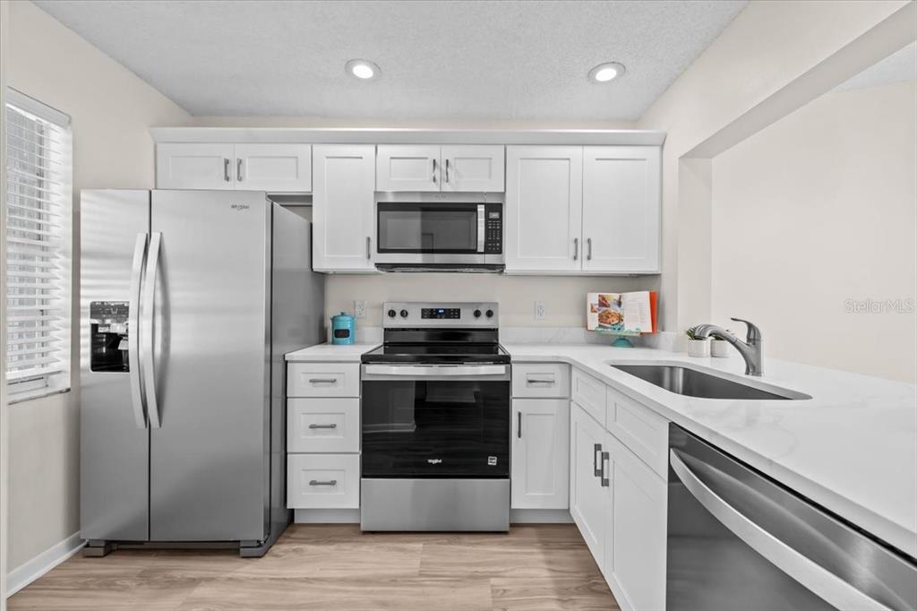 A kitchen features white cabinets, stainless steel appliances, and light-colored countertops — 1390 OAK HILL DRIVE UNIT 202, DUNEDIN, FL