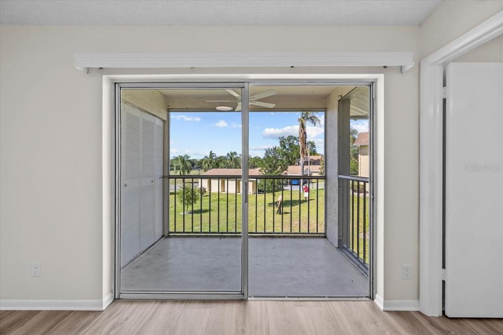 A room with light-colored walls and wood-look flooring features a sliding glass door to a balcony — 1390 OAK HILL DRIVE UNIT 202, DUNEDIN, FL