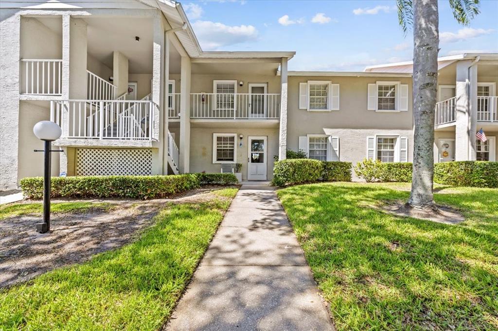 A concrete walkway leads to the entrance of a two-story apartment building with balconies — 1390 OAK HILL DRIVE UNIT 202, DUNEDIN, FL