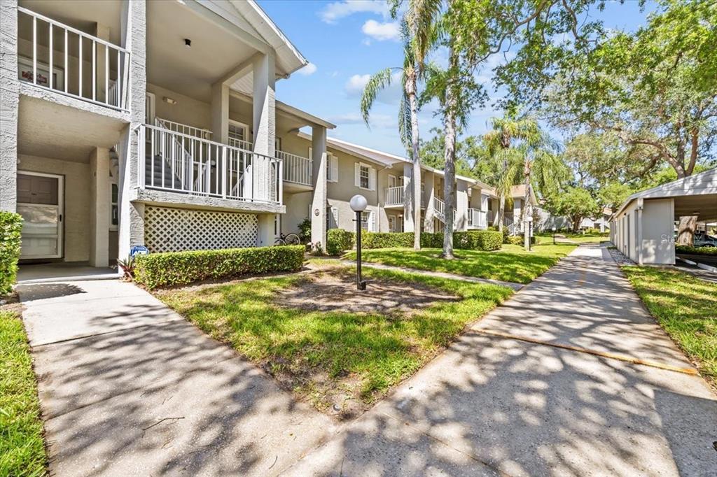 A multi-story apartment building with balconies, a concrete walkway, and landscaped green space — 1390 OAK HILL DRIVE UNIT 202, DUNEDIN, FL