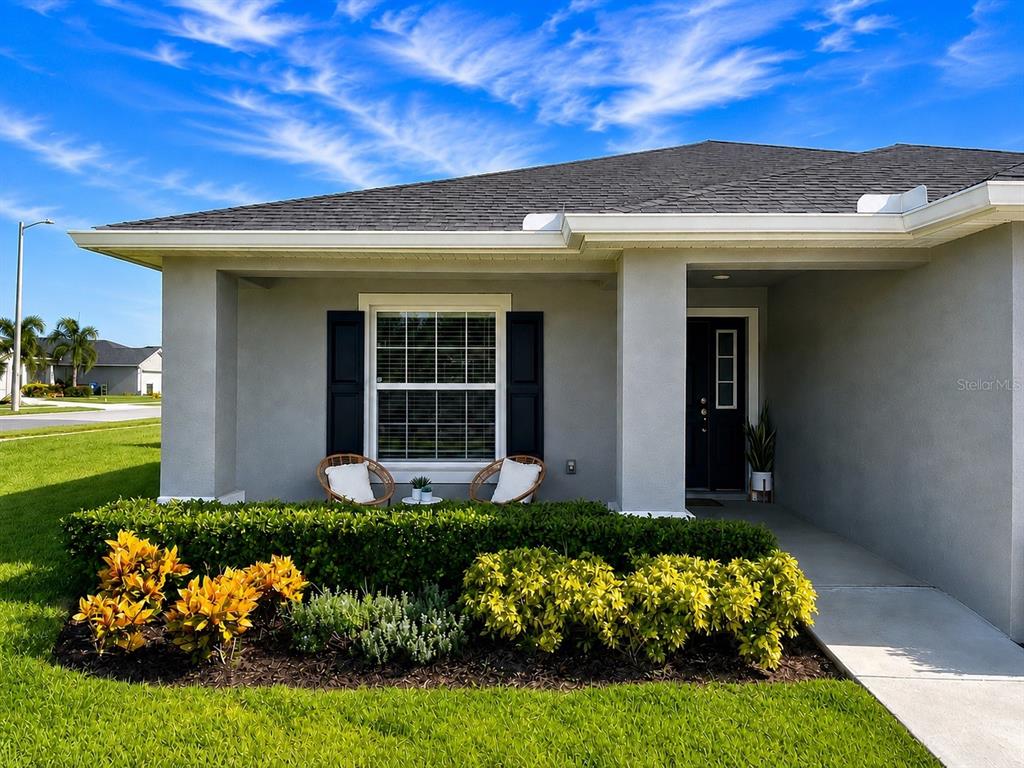 A gray house exterior features a covered porch with two chairs and manicured landscaping — 1002 PAISLEY STREET, LAKE ALFRED, FL
